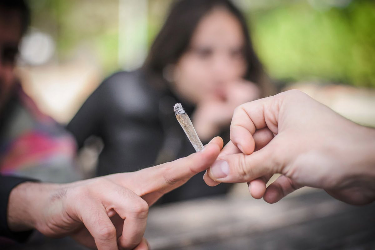 Close-up of a person passing a pre-roll joint to a friend
